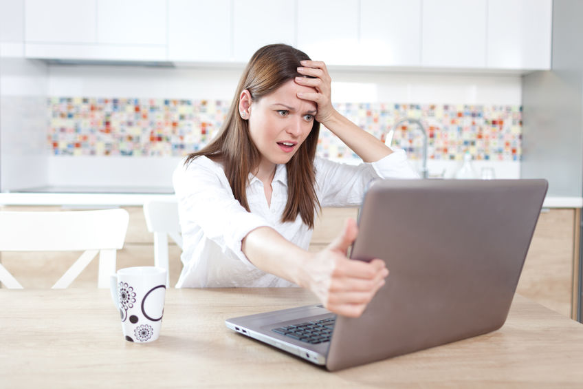 woman in her kitchen expressing frustration at her laptop computer