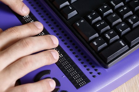  blind person using computer with braille computer display and a computer keyboard.