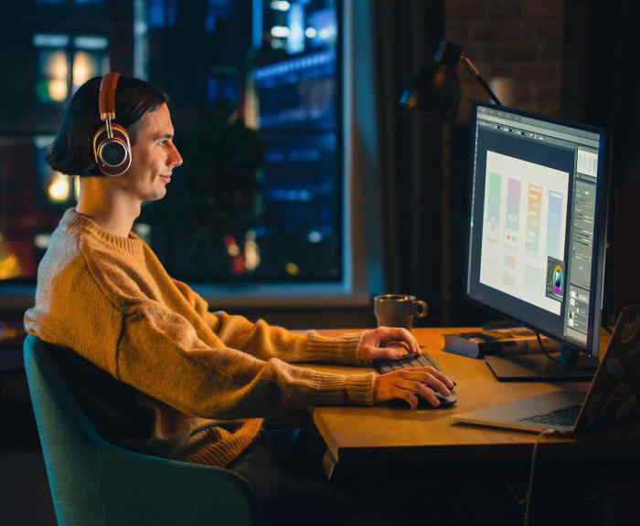 Person sitting at a computer desk with headphones on during the evening.